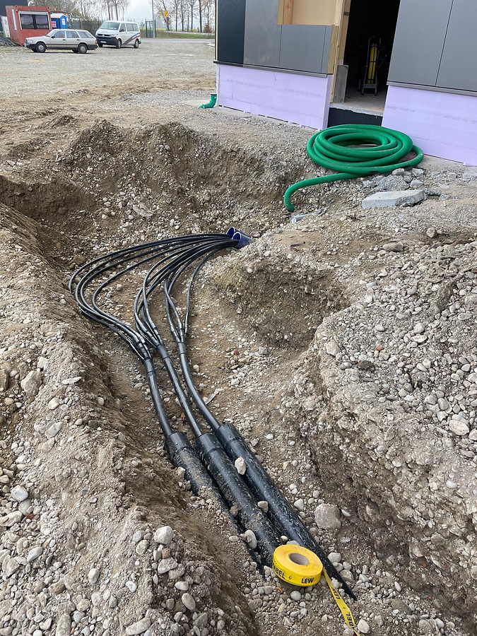 Mehrere Kabel laufen im offenen Graben zusammen, drei Muffen, daneben der Übergang ins Leerrohr am Hausanschluss