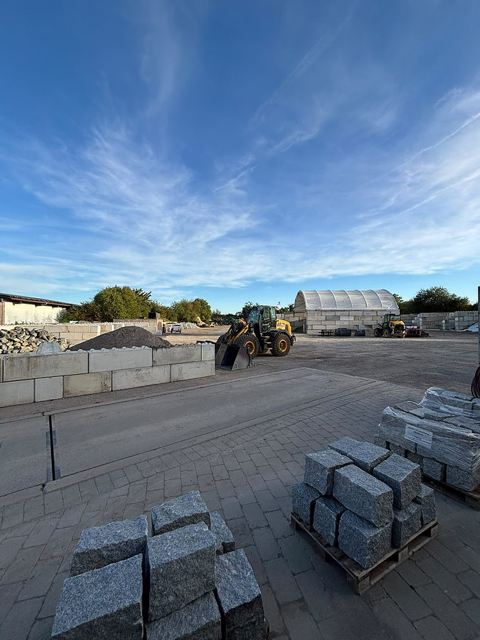 Radlader zwischen den Betonboxen des Lagerplatzes Bellenberg, vorn Granitsteine auf Paletten